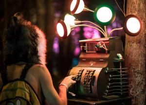 A guest plays with a piece of interactive art. It's base is an old cash register and there are lights of different colours coming out the top.